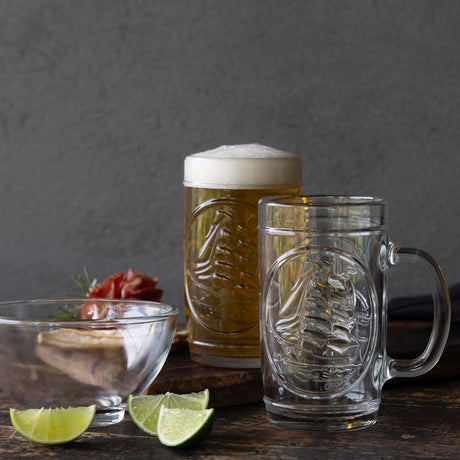 Dos vasos cerveceros con grabado del ARC Gloria en relieve, uno lleno de cerveza con espuma, sobre mesa rústica de madera con limones, bowl de vidrio y snacks
