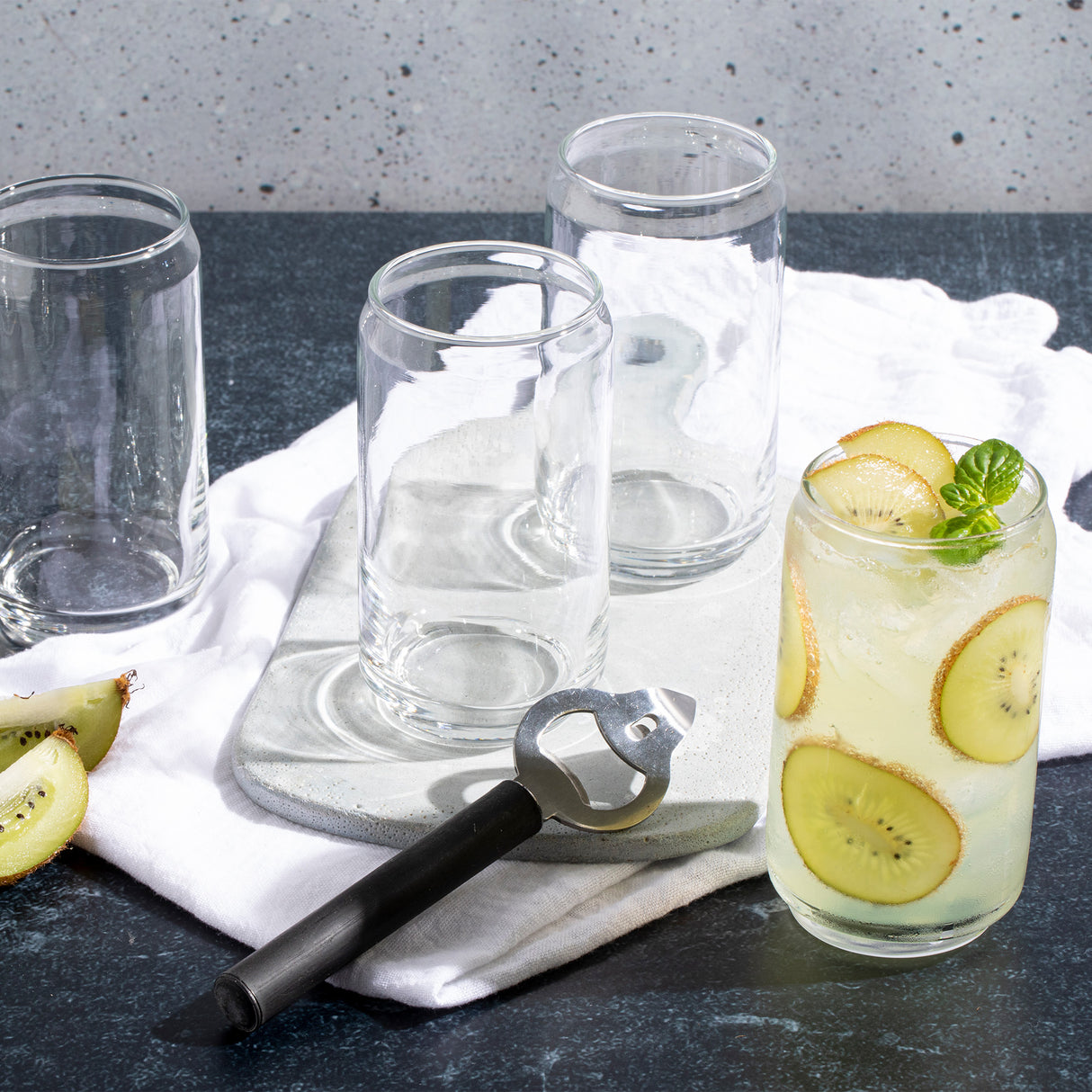 Cuatro vasos lata: un vaso de vidrio con bebida refrescante de kiwi, tres vasos vacìos