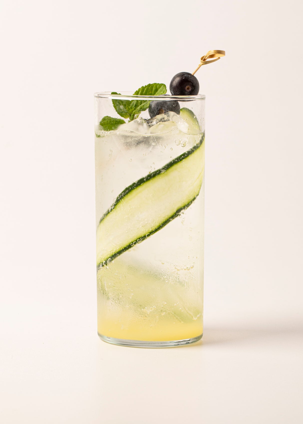 Vaso Río con una bebida refrescante de color claro, decorada con una tira de pepino en espiral, hojas de menta y una uva negra ensartada en un palillo.