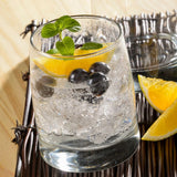 Vaso de vidrio  Toledo rocks con bebida, hielo, arándanos, rodaja de naranja y hojas de menta sobre una base de mimbre