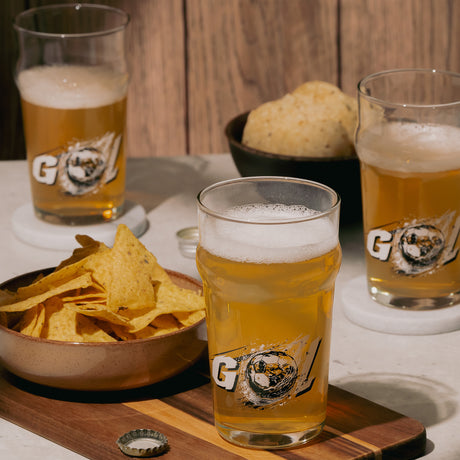 Tres vasos de vidrio Britain con cerveza espumosa, acompañados de snacks