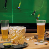 Cerveza servida en dos vasos altos junto a palomitas, papas fritas y frutos secos en mesa de madera